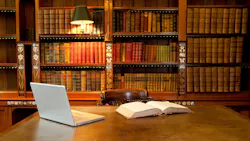 book and laptop on table with wall of books behind the table. subdued lighting book and laptop on table with wall of books behind the table. subdued lighting