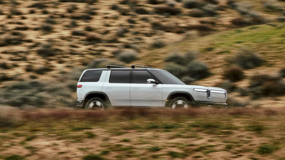 White Rivian R2 driving in dry looking area.