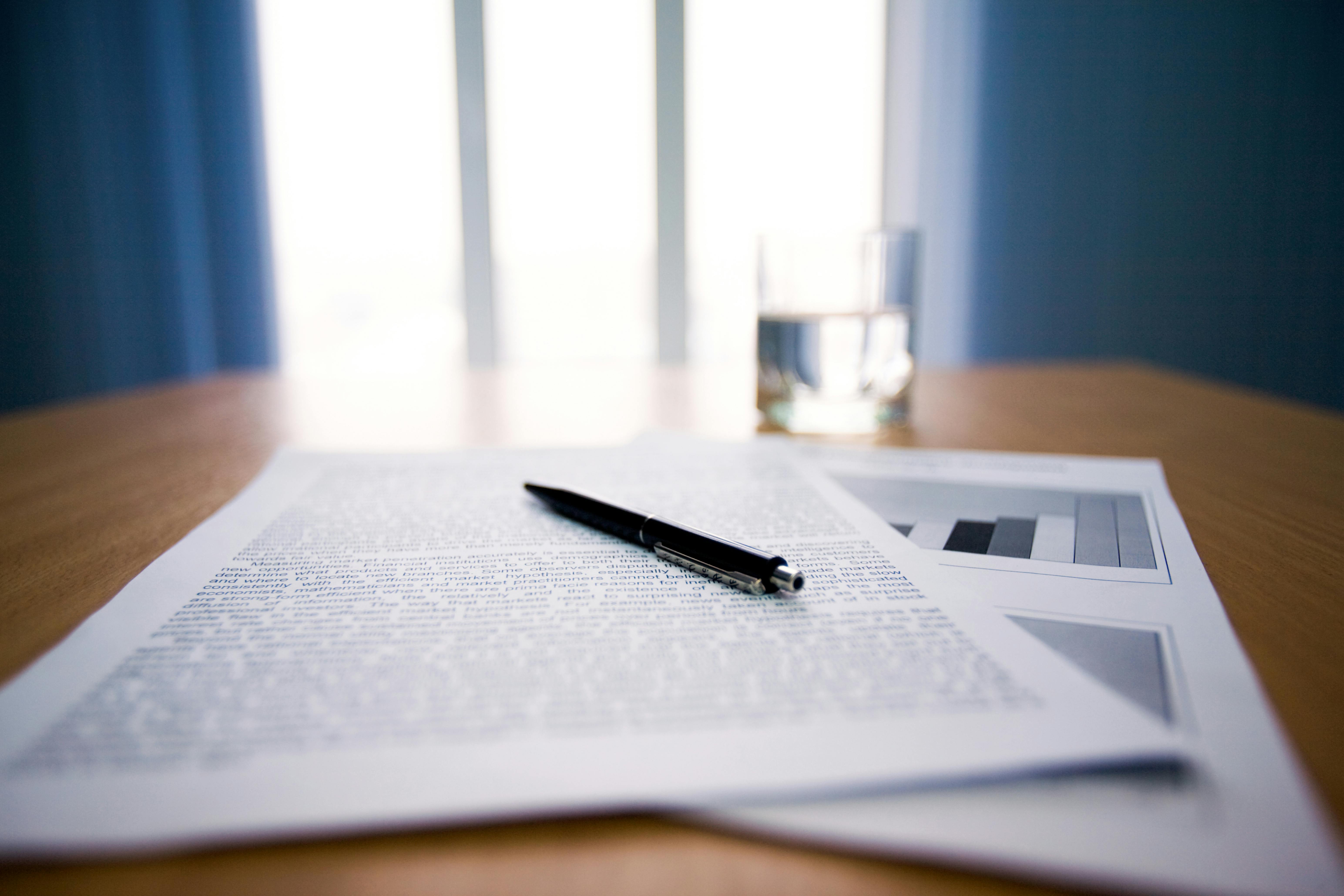 Image of workplace with focus on papers and pen on the table
