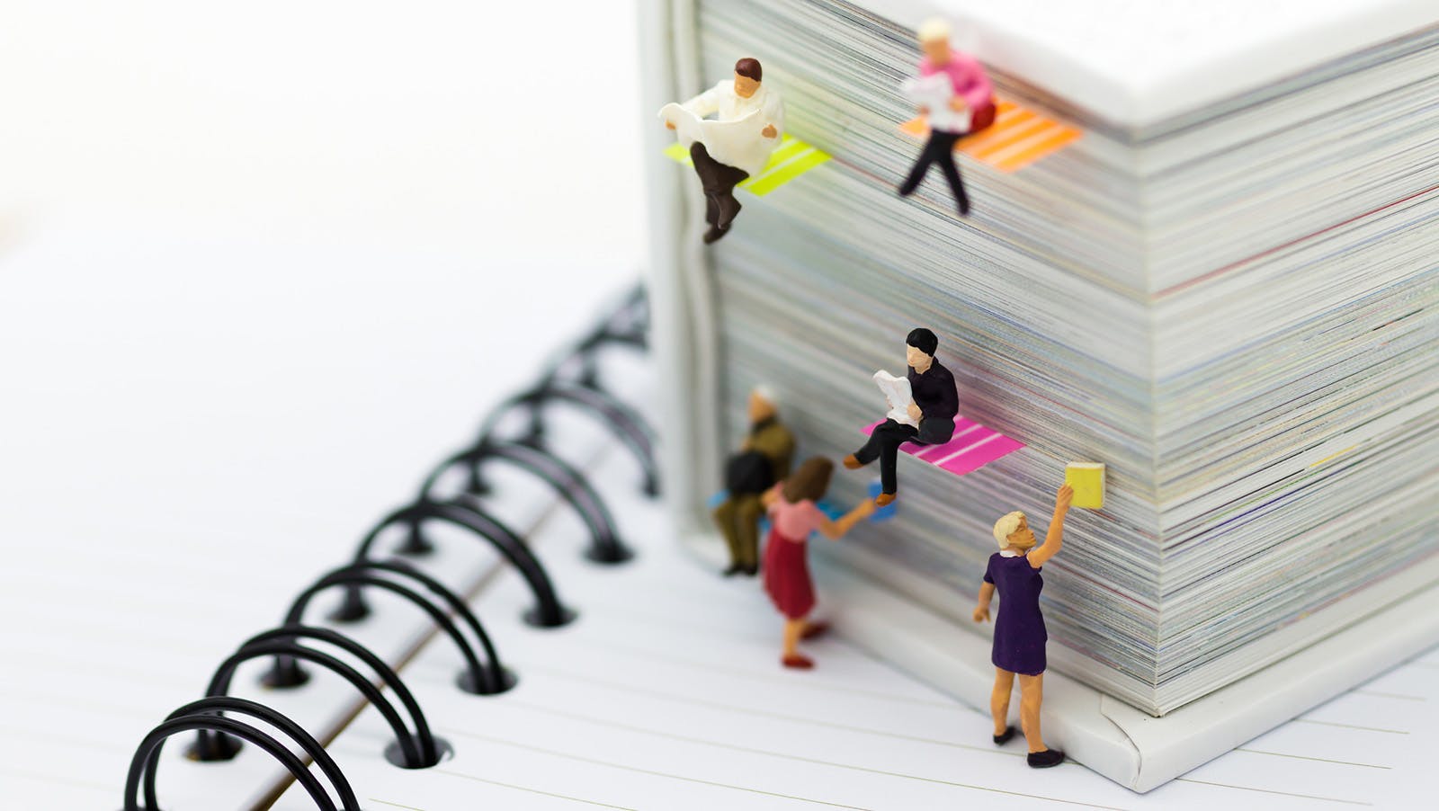 Miniature people reading newspapers on a big book