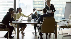 Company executive giving papers to employees at group meeting Company executive giving papers to employees at group meeting