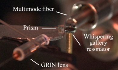 A gradient-index (GRIN) lens supplies IR light to a diamond prism that couples the light into a lithium niobate whispering-gallery resonator. The generated near-IR, visible, and UV light are collected by a multimode fiber.