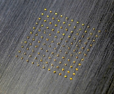 Small gold spots are laser-clad onto stainless steel.