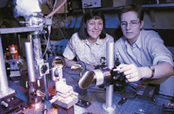 Researchers Deborah Sivco (top left) and Claire Gmachl (top right) monitor a lab experiment containing a bidirectional semiconductor laser. A two-wavelength version of the laser emits light at 6.33 µm with a positive bias and 6.5 µm with a negative bias; wavelength varies with temperature (bottom). Longitudinal mode structure spans a width of 0.3-0.5 nm. Researchers Deborah Sivco (top left) and Claire Gmachl (top right) monitor a lab experiment containing a bidirectional semiconductor laser. A two-wavelength version of the laser emits light at 6.33 µm with a positive bias and 6.5 µm with a negative bias; wavelength varies with temperature (bottom). Longitudinal mode structure spans a width of 0.3-0.5 nm.