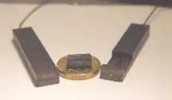 Polymer-encapsulated lasers contain rhombic Nd:YAG laser crystals (visible by the greenish reflection from their thin-film coatings). A fully encapsulated laser 50 × 10 × 3 mm in size with fiber-pump source is at left; the partly encapsulated laser at right was used in the experiments. The laser at center has no fiber-pump source. The coin seen at center as a size reference is a Swedish 10-kronor coin 20.5 mm in diameter. Polymer-encapsulated lasers contain rhombic Nd:YAG laser crystals (visible by the greenish reflection from their thin-film coatings). A fully encapsulated laser 50 × 10 × 3 mm in size with fiber-pump source is at left; the partly encapsulated laser at right was used in the experiments. The laser at center has no fiber-pump source. The coin seen at center as a size reference is a Swedish 10-kronor coin 20.5 mm in diameter.