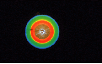 FIGURE 1. Light is produced by the process of parametric downconversion in which photons input into a nonlinear crystal, in effect, decay into pairs of photons under the constraints of energy and momentum conservation. In this particular case, a laser beam at 351 nm was sent into a KDP crystal. The central spot is a small amount of 351-nm light leaking around a beam stop. For the case in which the input photons split frequency evenly, two photons at 702 nm (red) are produced; the process also produced other pairs consisting of photons redder and bluer than 702 nm.