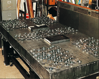 To verify the effectiveness of a distributed tuned mass damping system, 350 individual dampers distributed in frequency were applied to the corners and center region of an optical table. The masses of the dampers totaled 37 kg; no tuning was involved. In the commercial version, fewer dampers wil be used, and the dampers will be mounted inside the table structure. The rectangular objects are 55-lb masses used to load the table.