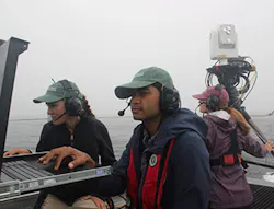 Johns Hopkins University Applied Physics Laboratory (APL) free-space optical (FSO) operators check the monitors on Sea Hunter as a third operator monitors operations. The FSO system can be seen at top right. Johns Hopkins University Applied Physics Laboratory (APL) free-space optical (FSO) operators check the monitors on Sea Hunter as a third operator monitors operations. The FSO system can be seen at top right.