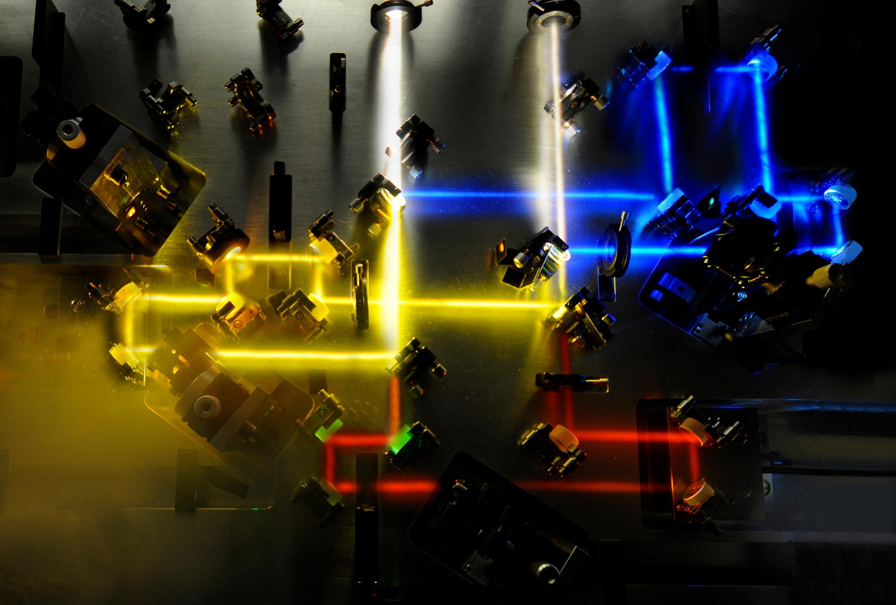 A photonic system produces custom-shaped sub-femtosecond light transients used to probe the behavior of electrons within atoms. To create the transients, a supercontinuum is first divided into three channels (seen as blue, yellow, and red); beam parameters for each channel are manipulated before recombining the light (white).