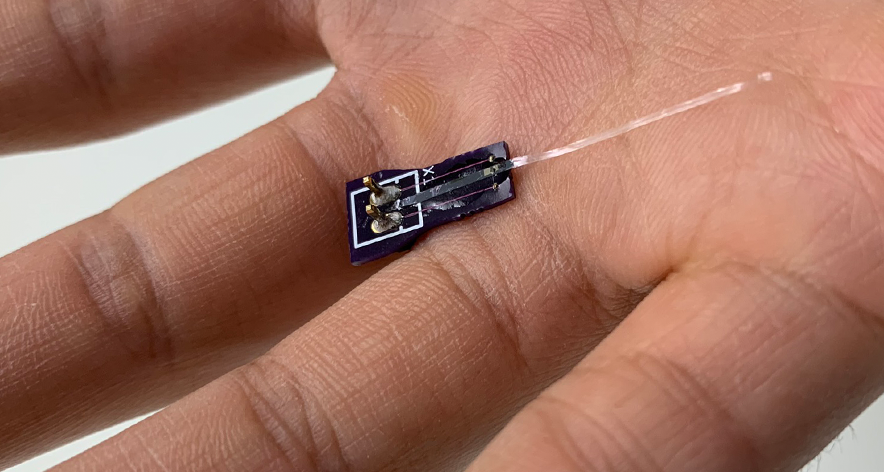A Parylene C photonic waveguide is held in the hand for scale.