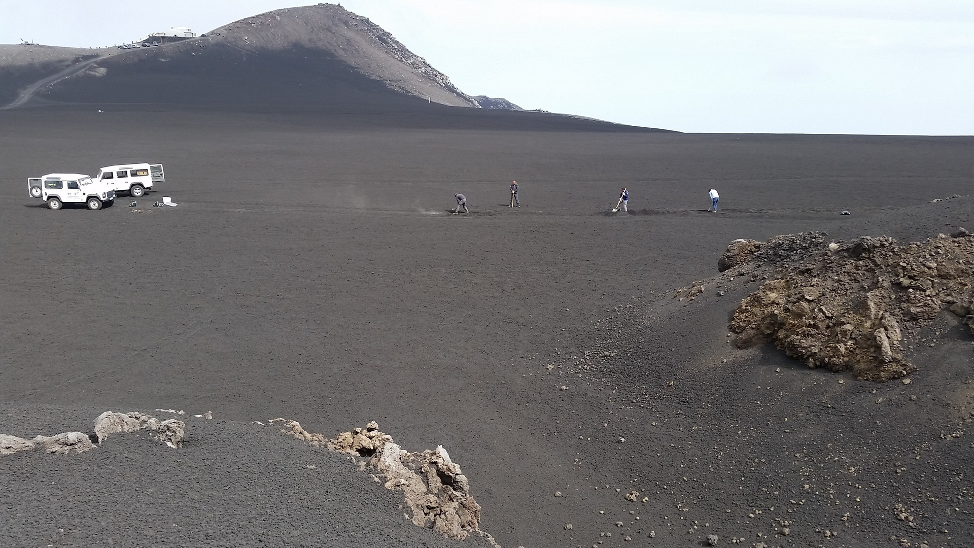 FIGURE 1. Researchers dig the trench for the fiber-optic cable at the site of Mount Etna (2800 m elevation, Piano delle Concazze; the Pizzi Deneri Observatory can be seen in the background.