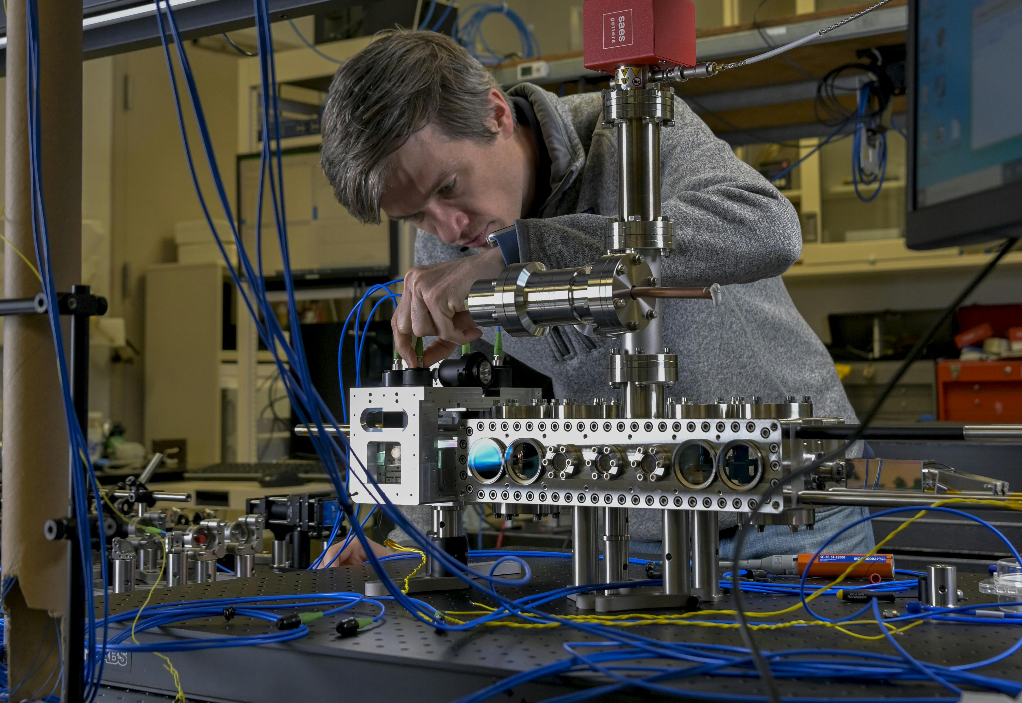 Jonathan Kwolek attaches fiber-optic cables to send light into a compact laser system, which is aligned around a custom vacuum cell. It generates a cold, continuous atomic beam, which is delivered to a larger vacuum chamber to address the Navy&rsquo;s inertial navigation challenges.