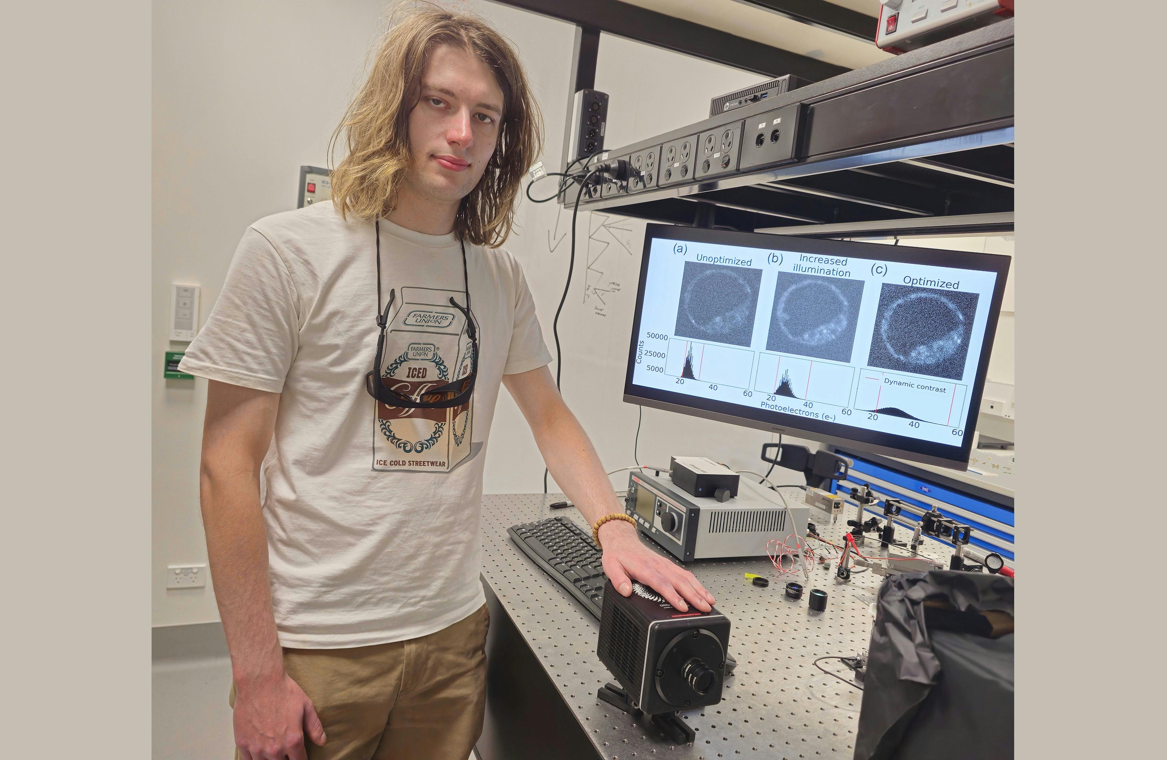 Ph.D. student Zane Peterkovic with a photon-counting camera; the screen behind displays the improvement in quality possible with camera optimization.