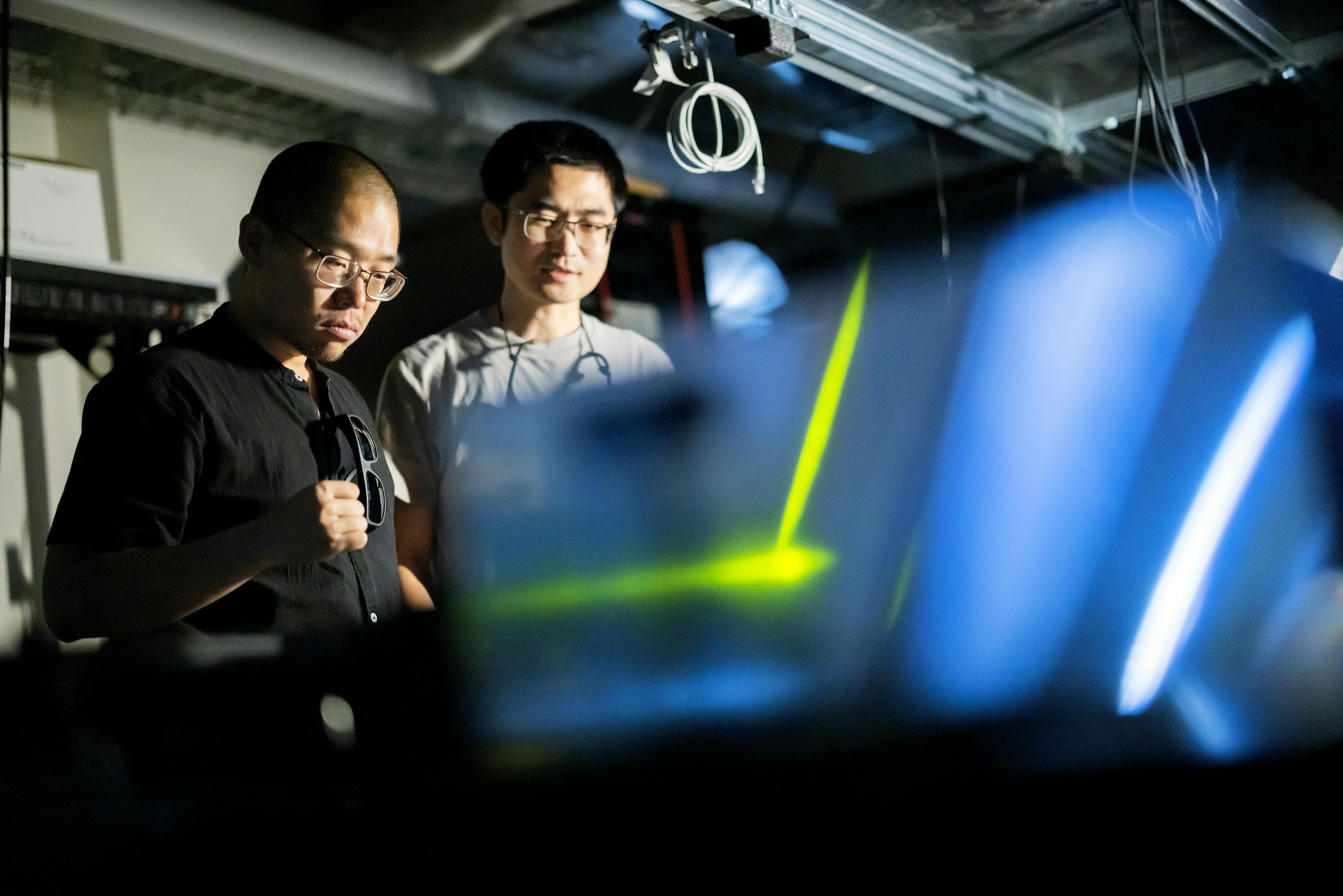 FIGURE 1. Li He (left) and Bo Zhen (right) in the lab with their photonic crystal platform that enables guiding light in a forward-only direction around a chip&rsquo;s defects and bends. Credit: Eric Sucar/University of Pennsylvania