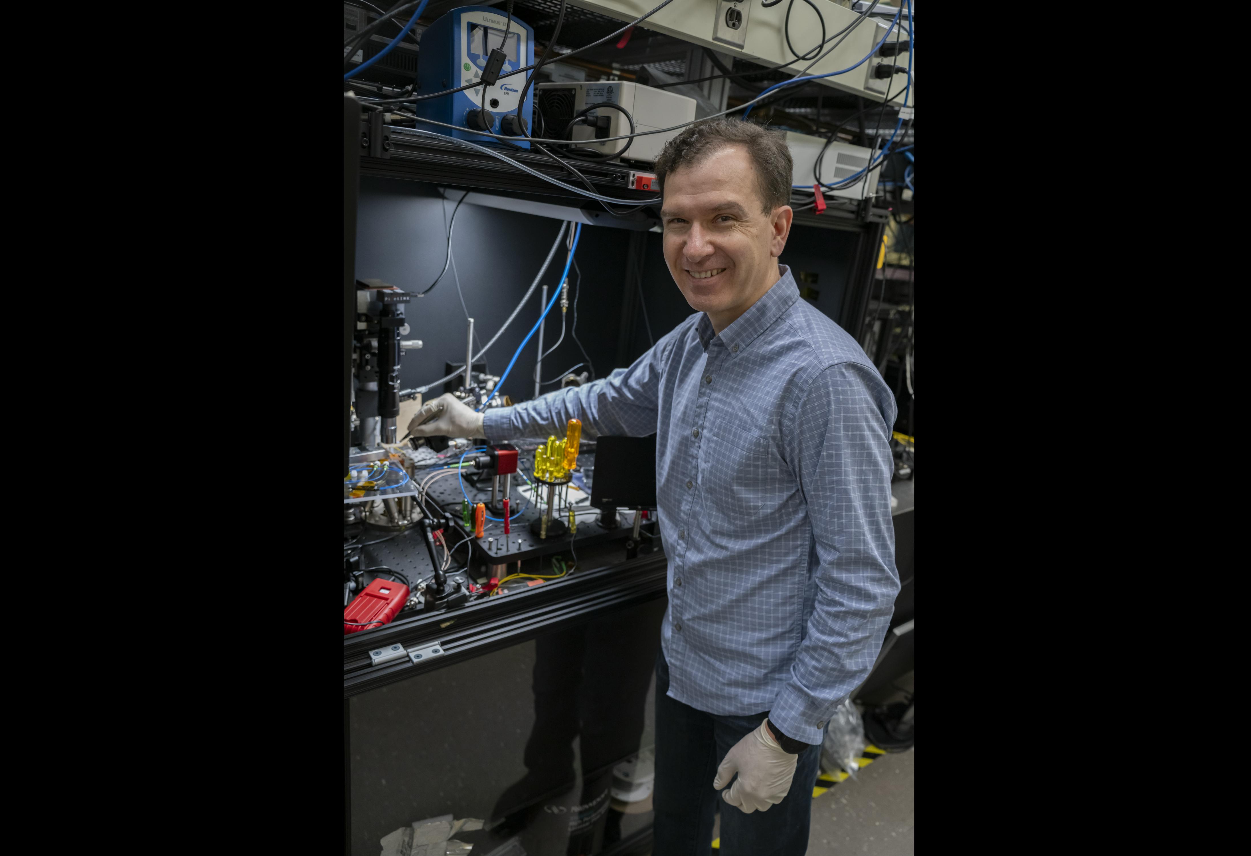 NIST scientist Nikolai Klimov holds a PIC with tweezers.
