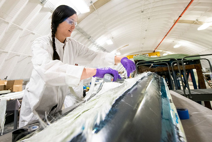 Robynne Murray, chercheuse au NREL, travaille sur une aube de turbine en composite thermoplastique au NREL.  Les thermoplastiques, contrairement aux thermodurcissables, peuvent être recyclés, ce qui rendrait l'énergie éolienne plus durable tout en réduisant les coûts.