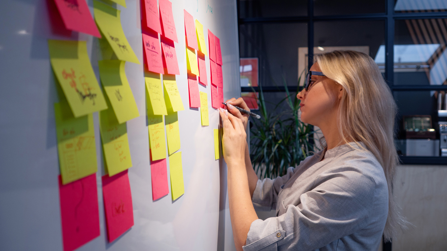 Person writing on a sticky note on a wall of notes