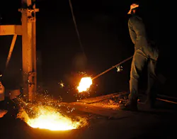 A worker in a factory making cast iron parts stands close to the melting pit. A worker in a factory making cast iron parts stands close to the melting pit.