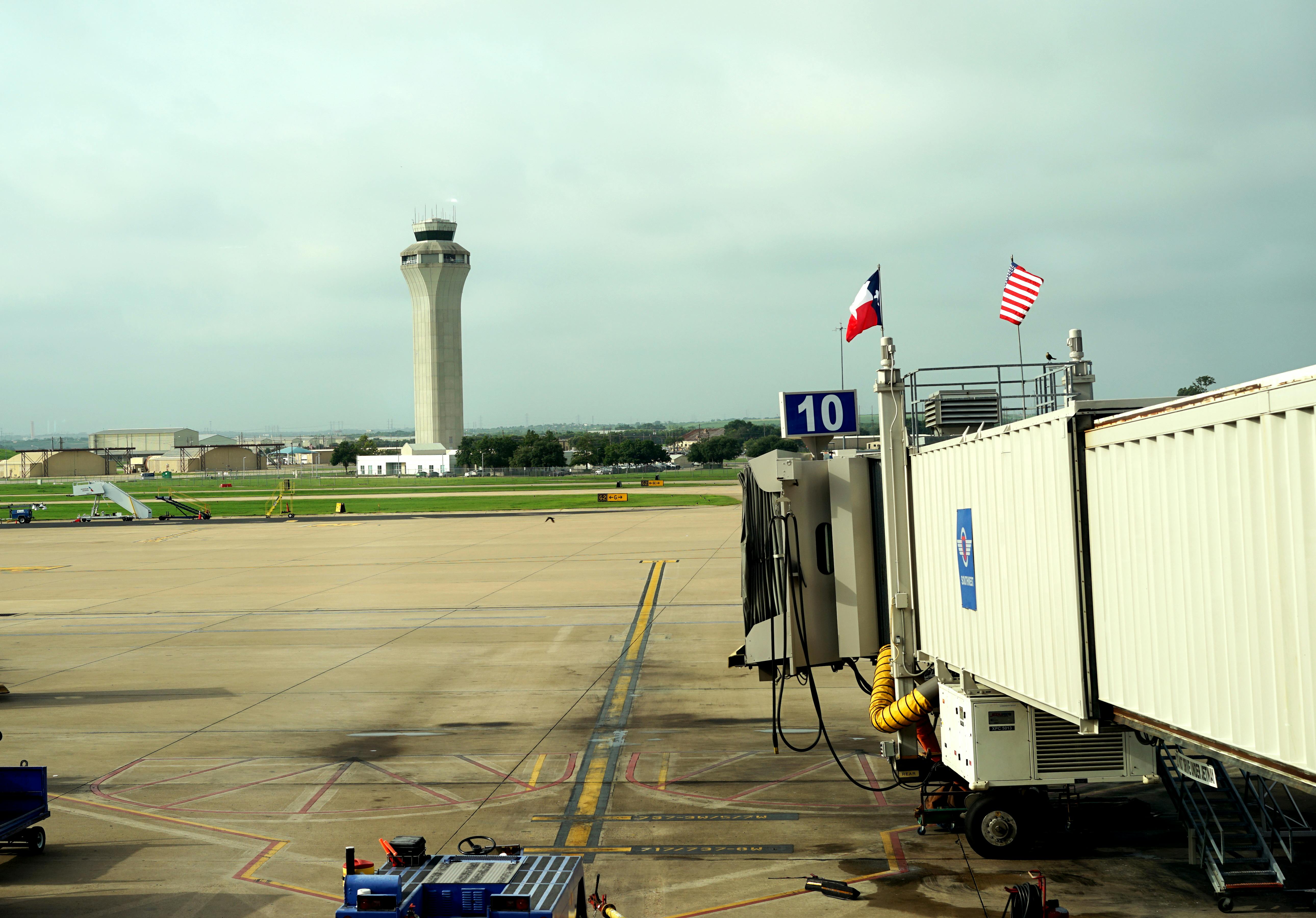 Texas and American flags fly above waiting jetway at Austin-Bergstrom airport. Air traffic control tower is in the background. Photo 56407993 &copy; Linda Williams | Dreamstime.com