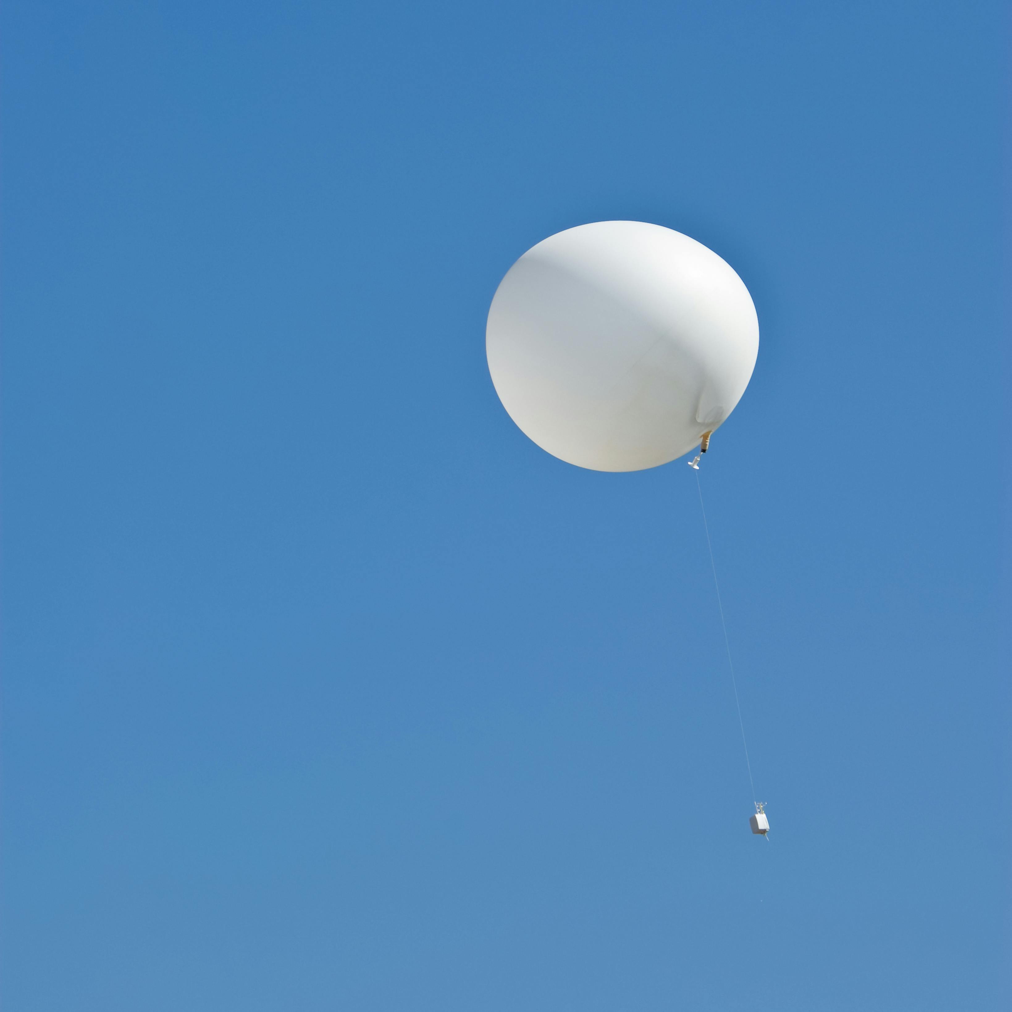 A weather balloon ascends amid a blue sky.