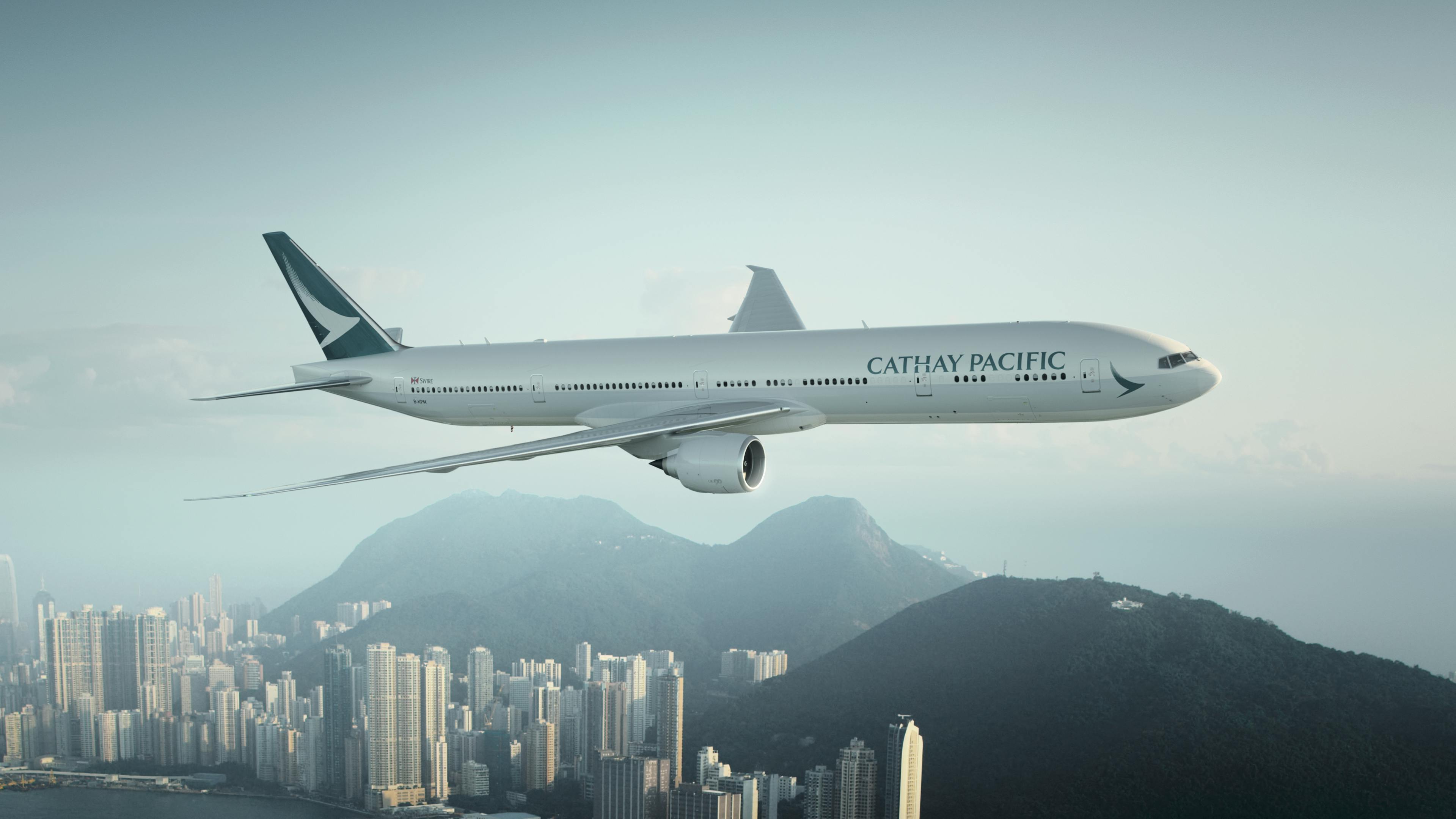 Cathay Pacific's 777 aircraft flies above a cityscape.