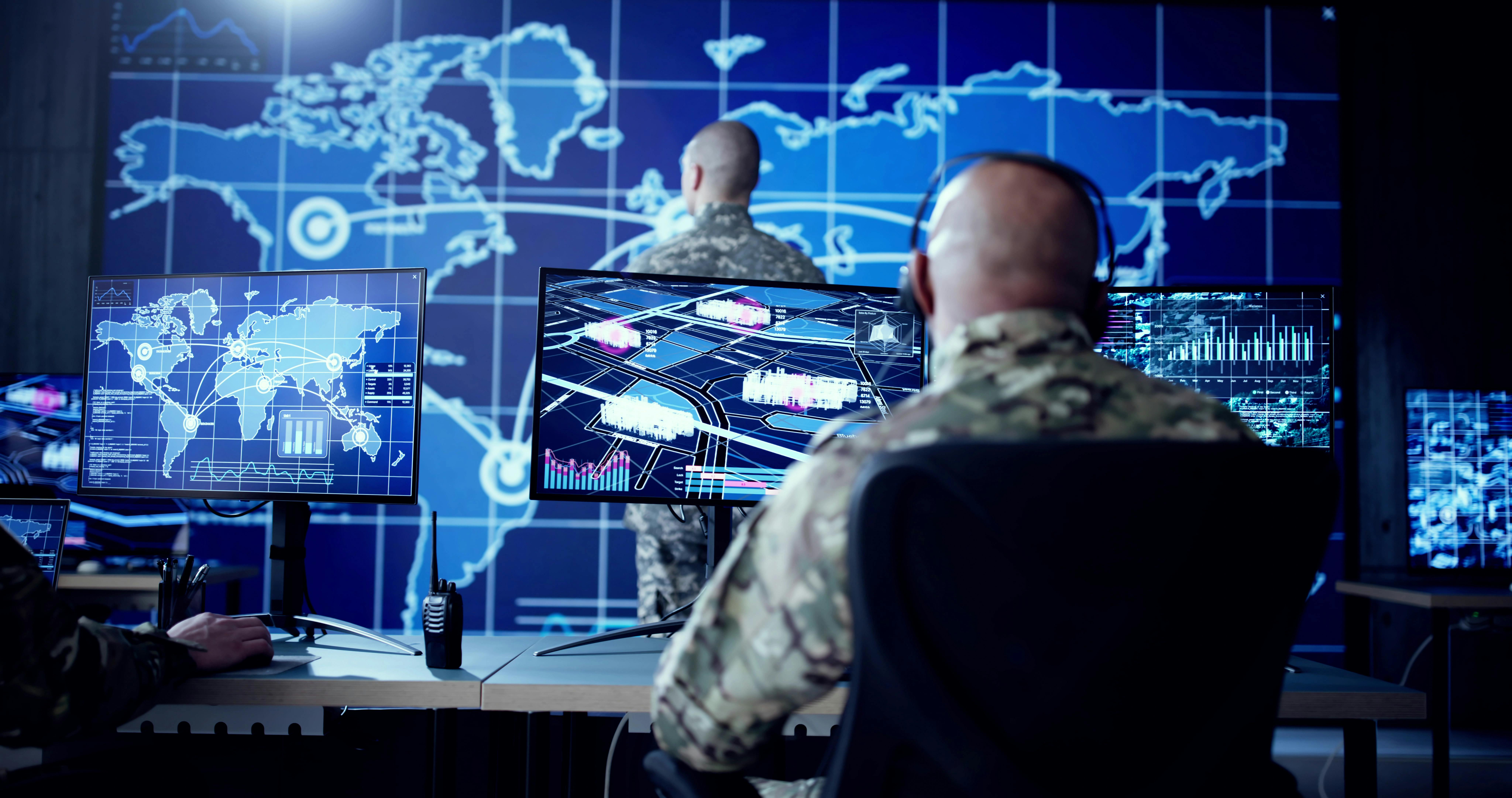 Cyber technology operator monitoring surveillance cameras in military control center.