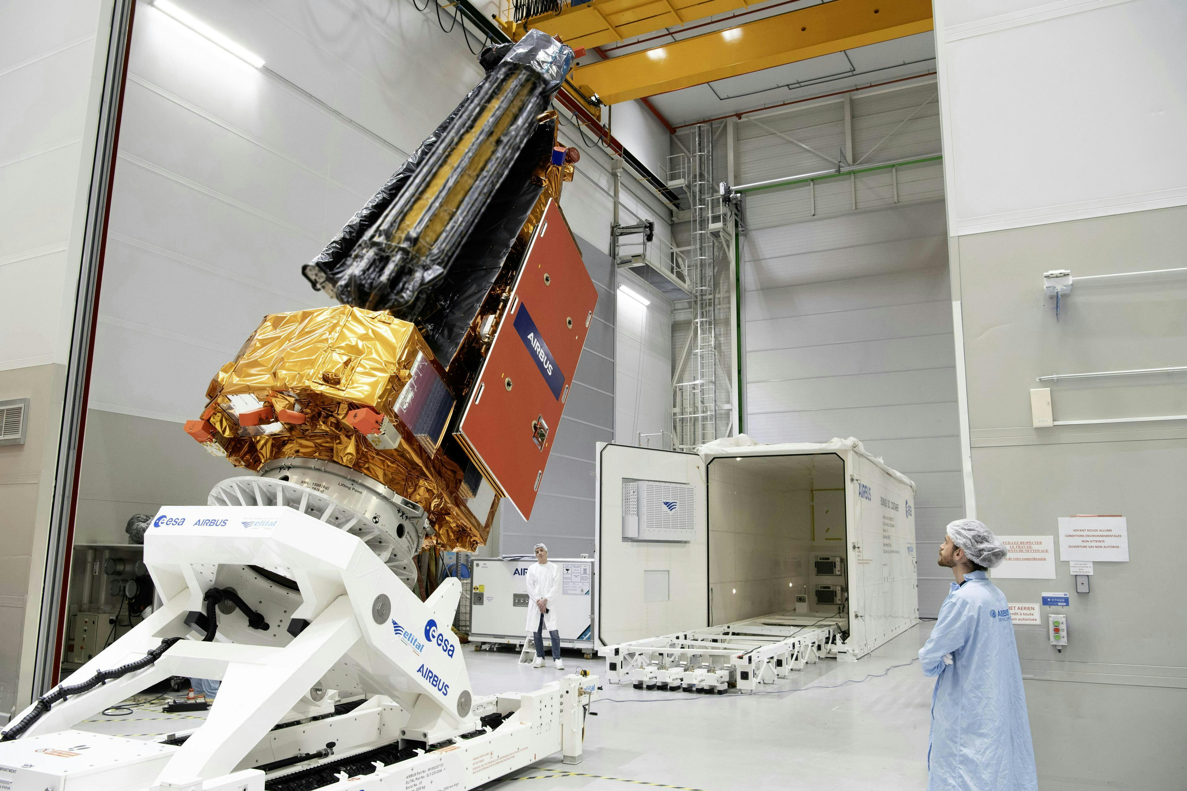 A person in a clean room watches the Biomass satellite prepared to be loaded into a container