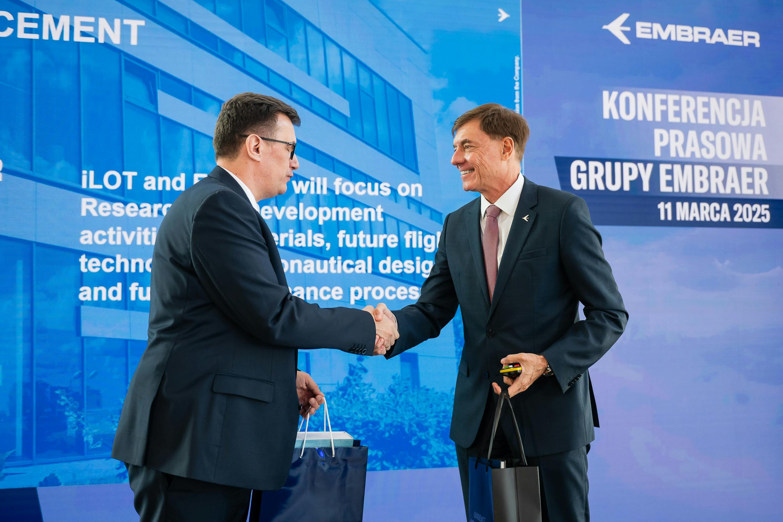 Representatives of Embraer and Lukasiewicz shake hands on a stage