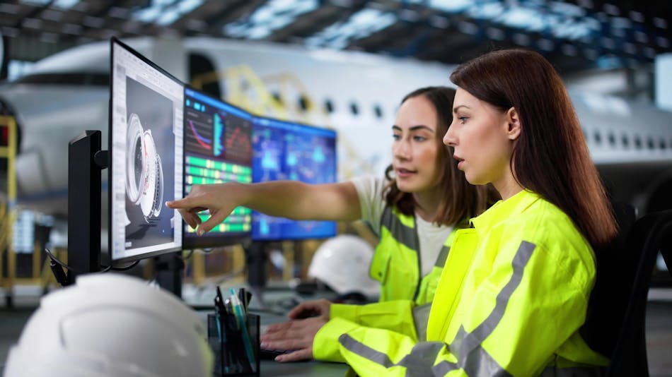 Two women look at a computer screen in an airplane hangar