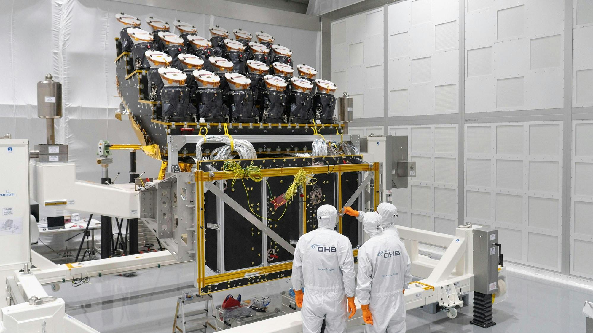 Three people in white clean suits in a clean room with the camera array