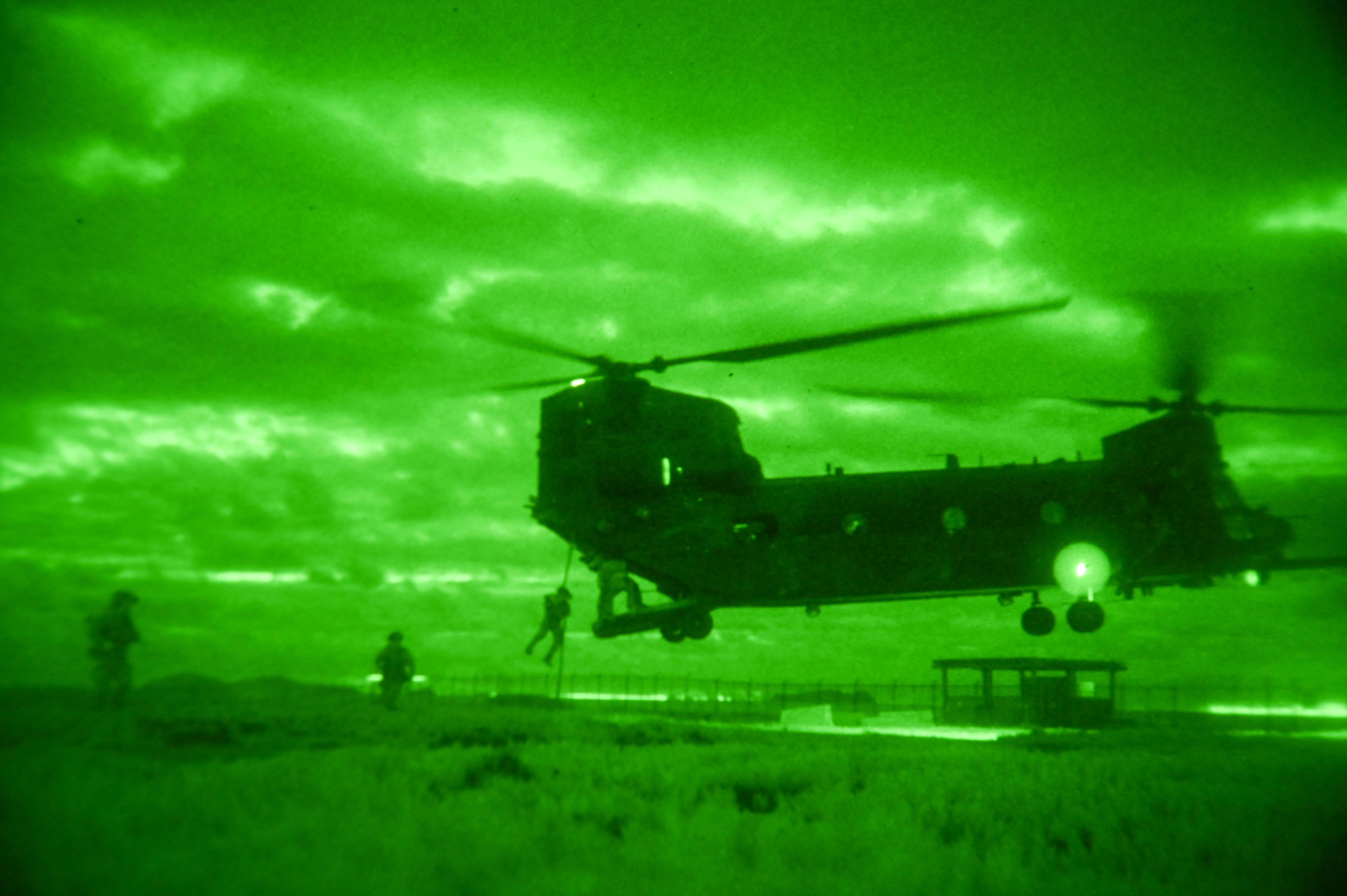 Naval Special Warfare (NSW) operators exit by fast rope from an MH-47G Chinook helicopter of the 160th Special Operations Aviation Regiment Night Stalkers while conducting nighttime helicopter roping suspension technique training.