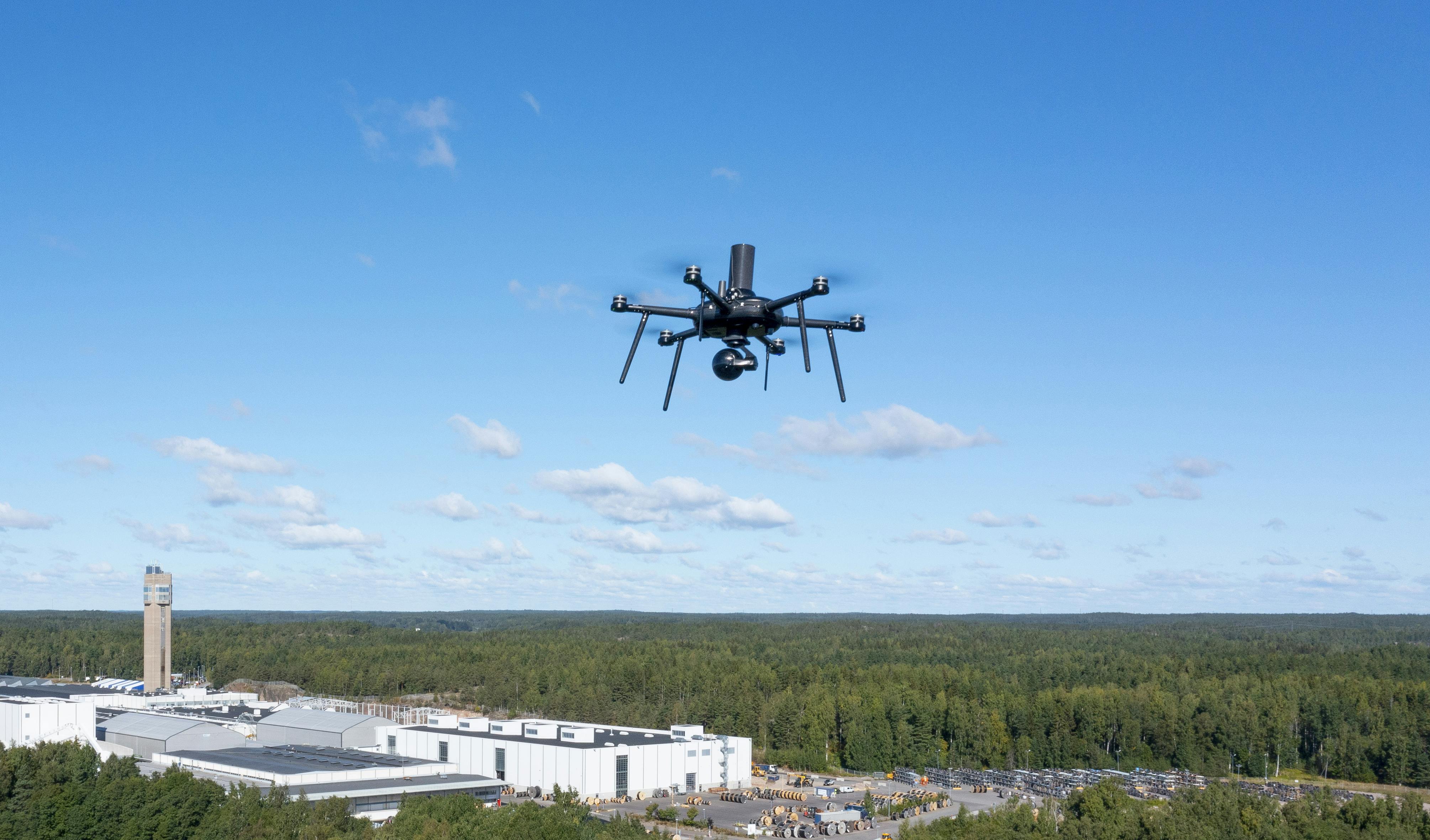 A small electric UAV flies at an industrial site.