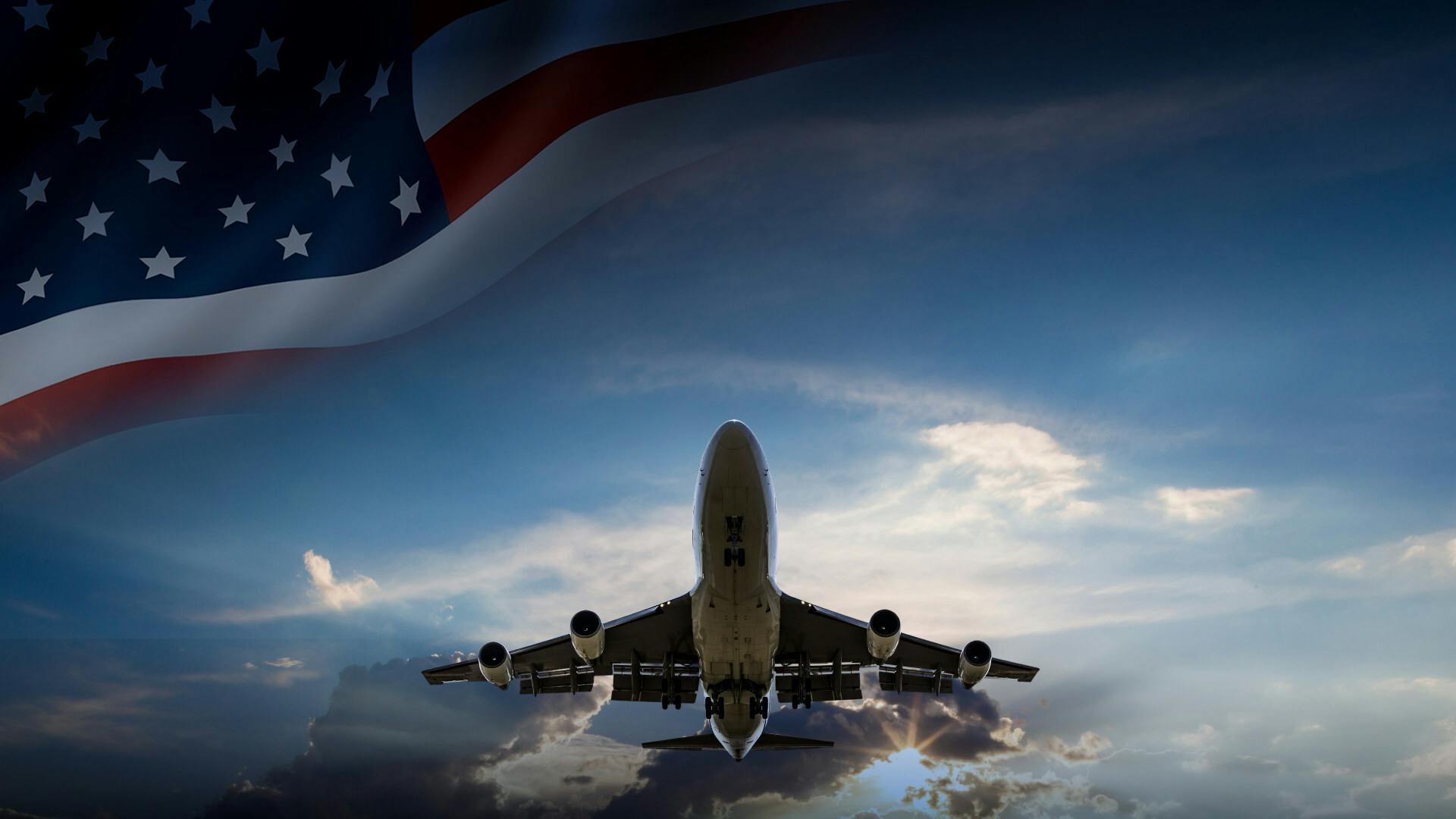 A commercial aircraft flying with a partial American flag waving above it.