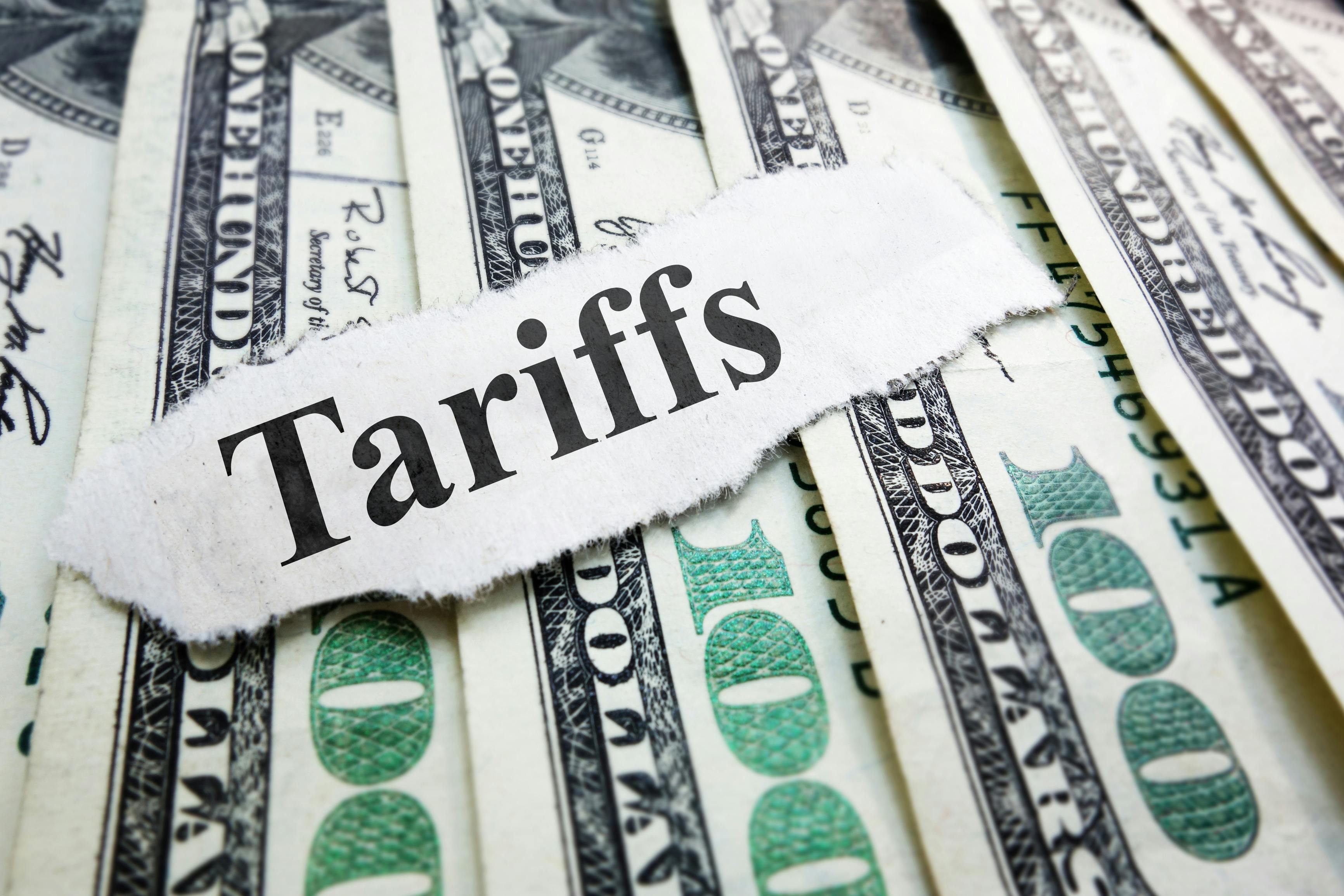 The word 'tariffs' atop spread out $100 U.S. bills.