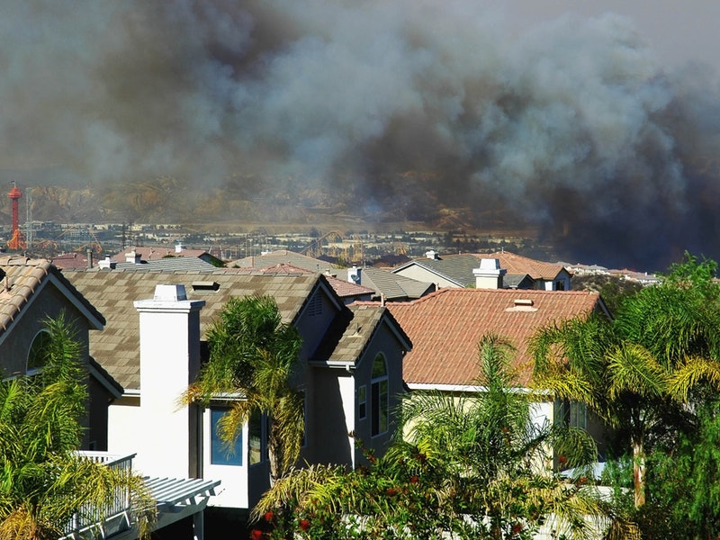 Smoke from an approaching wildfire can be seen hanging over a housing development in Southern California. By StacieStauffSmith Photos/Shutterstock.com