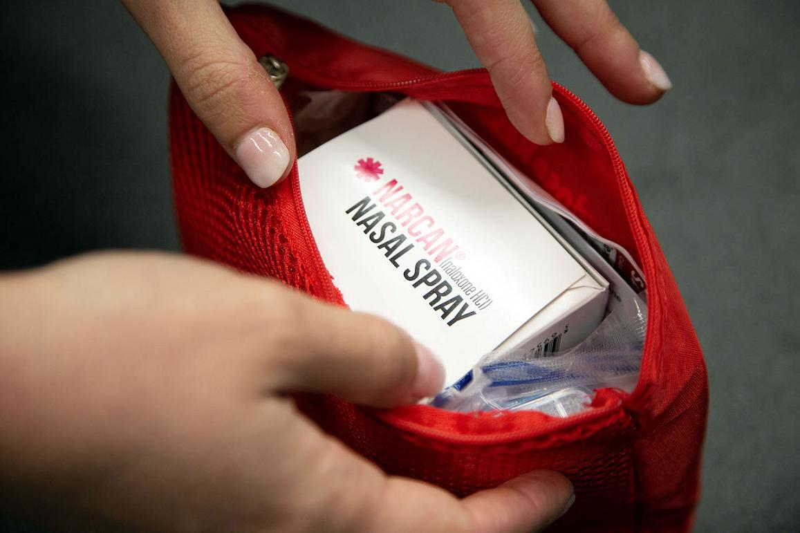 Close-up of a person's hands holding a red bag with a box of naloxone nasal spray inside. National Institute on Drug Abuse.