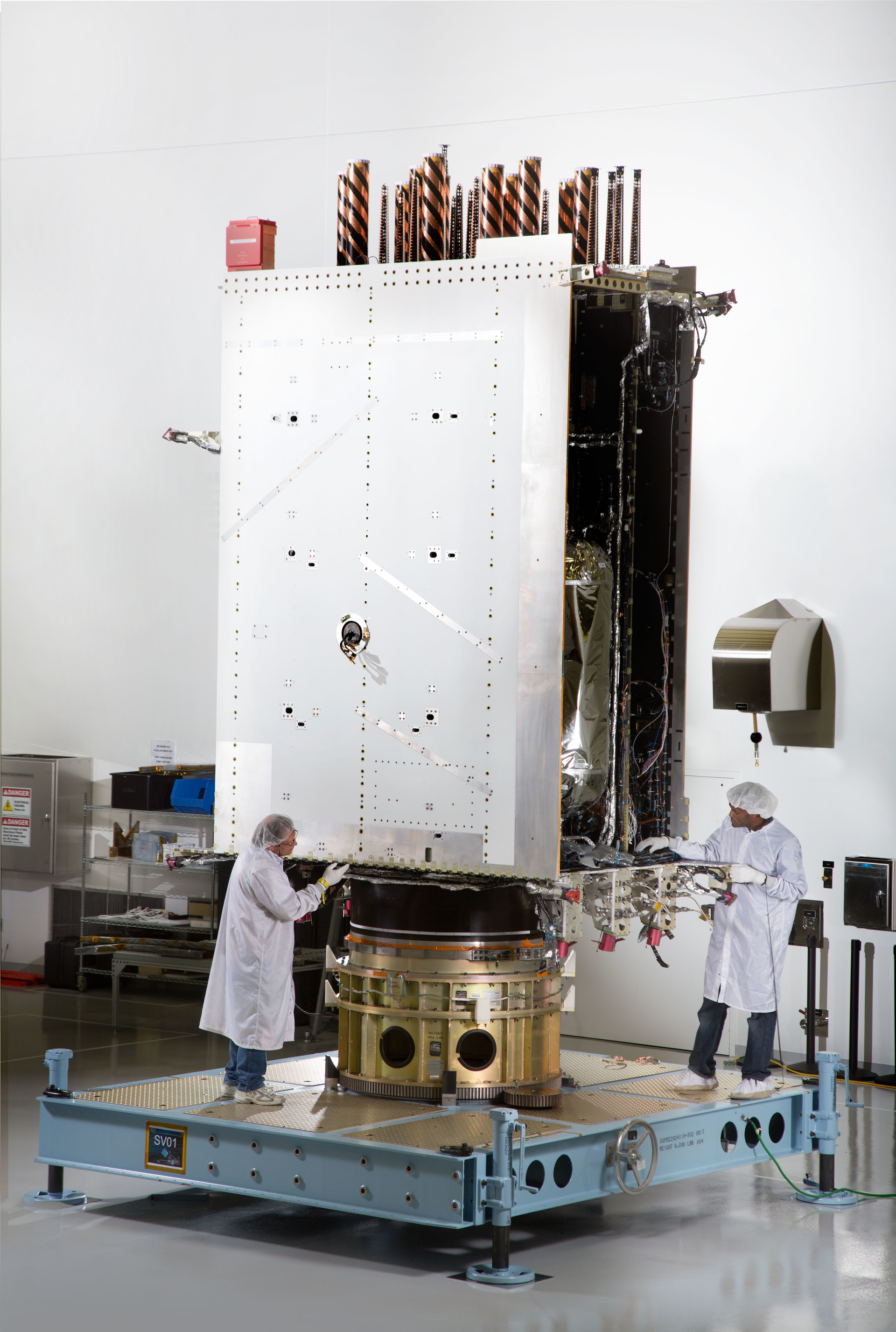Two engineers from Lockheed Martin prepare the first GPS III satellite for systemlevel testing at the companyrsquos Denverarea satellite facility earlier this year Image courtesy of Lockheed Martin