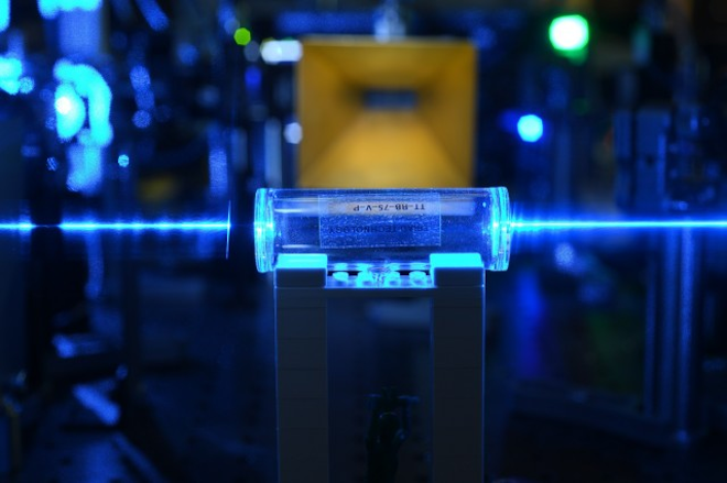 Atoms in a glass vapor cell are excited with laser beams to Rydberg states. They detect the electric fields coming from the gold antenna in the background and imprint the information back onto the laser beams.