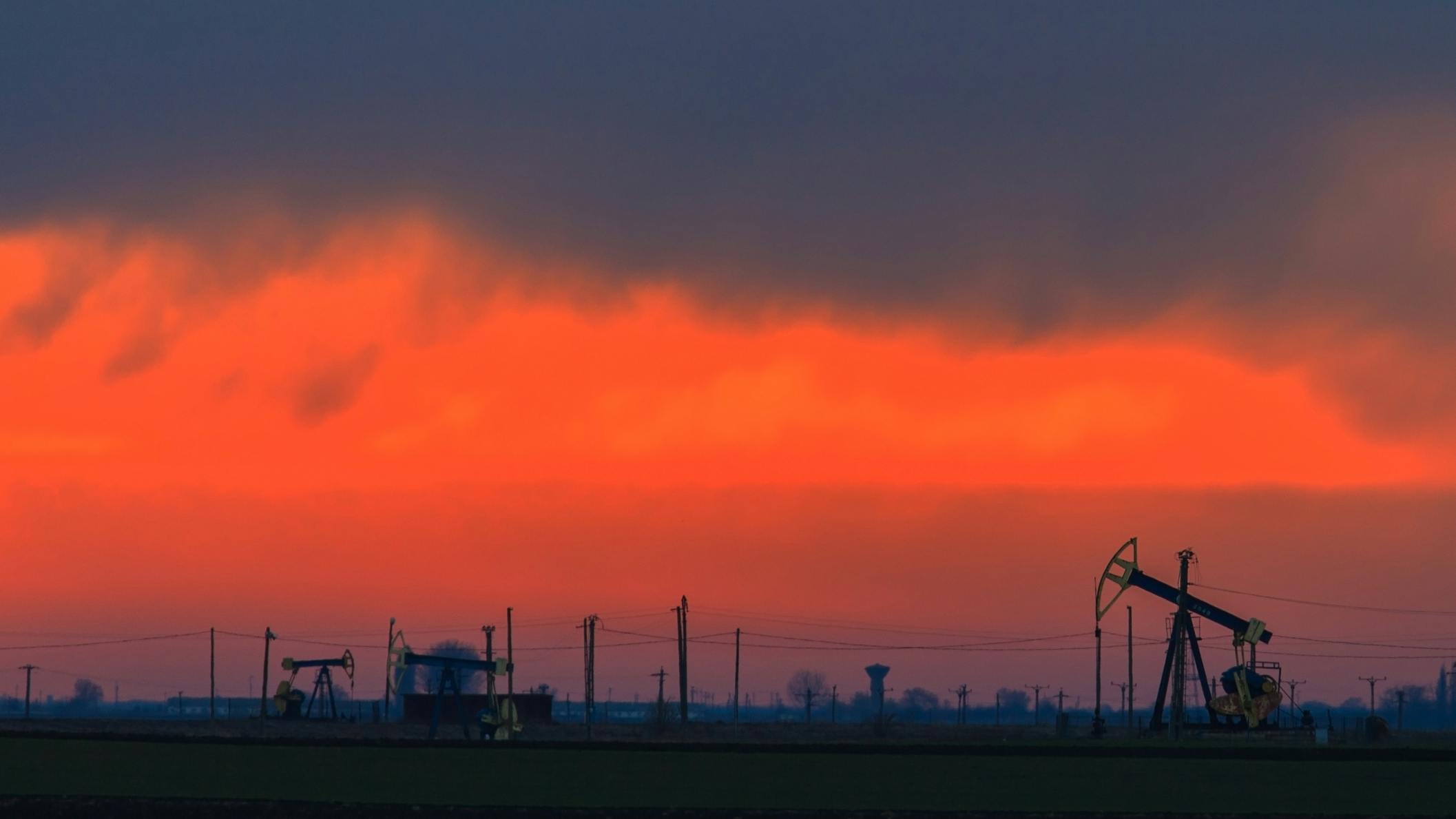 Oilfield with oil pumps and oil rigs profiled on sunset sky.