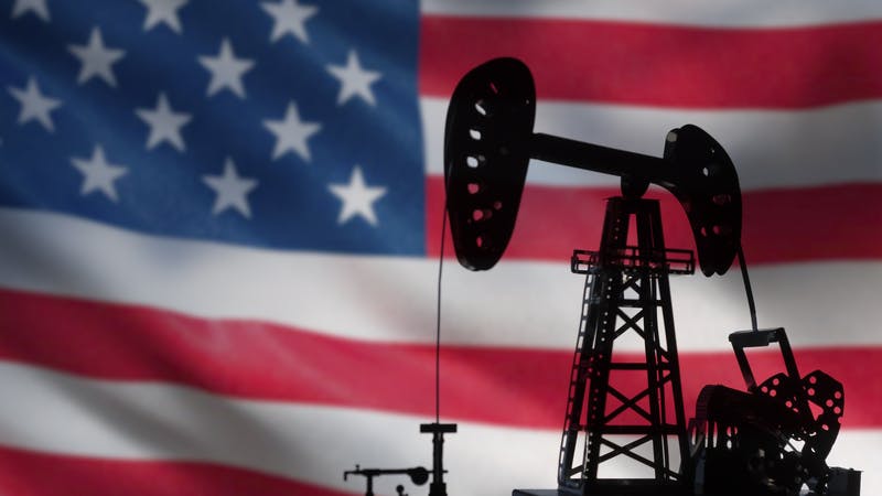 Silhouette of oil drilling pump on background of US flag.