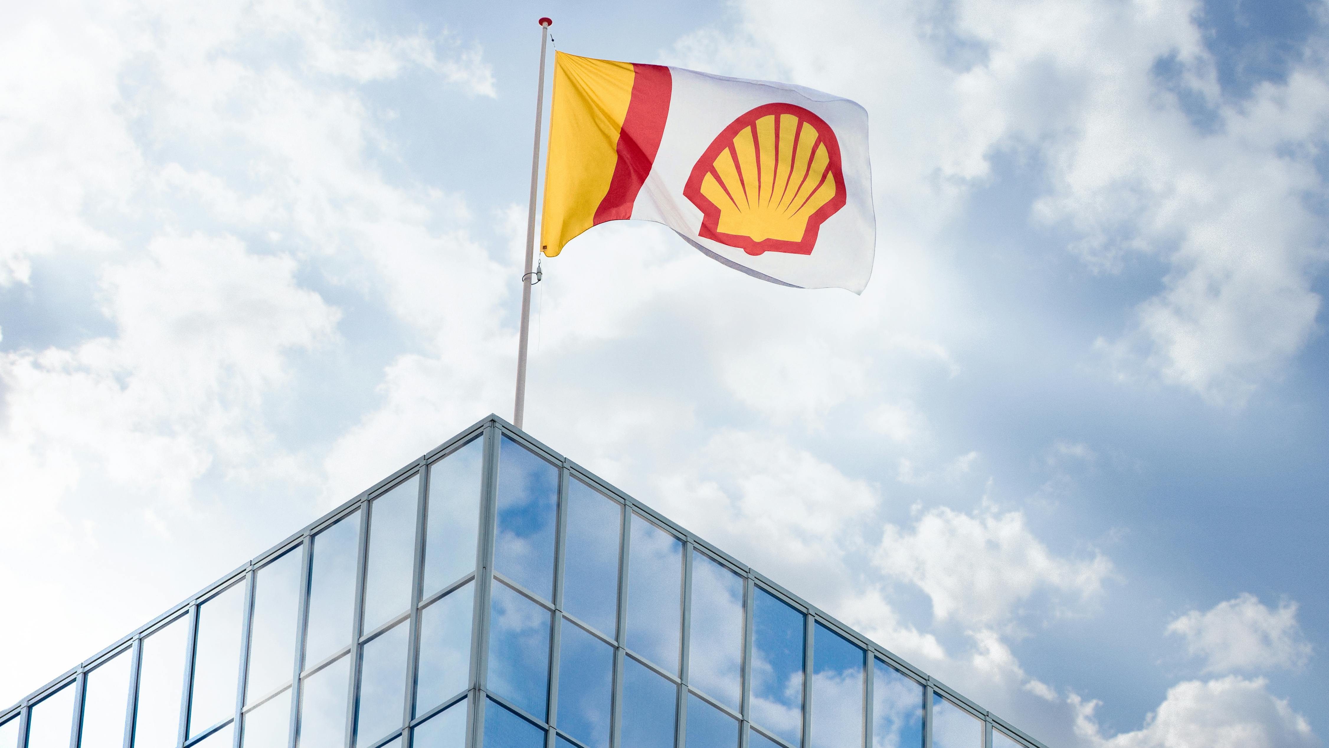 Shell flag flying on top of glass building against blue sky and cloud backdrop