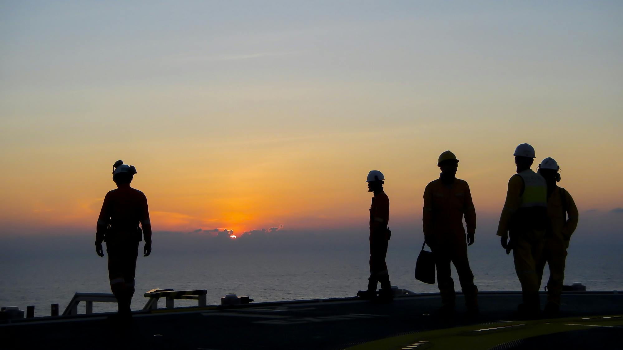 Silhouette of offshore oil and gas workers on helideck during sunset