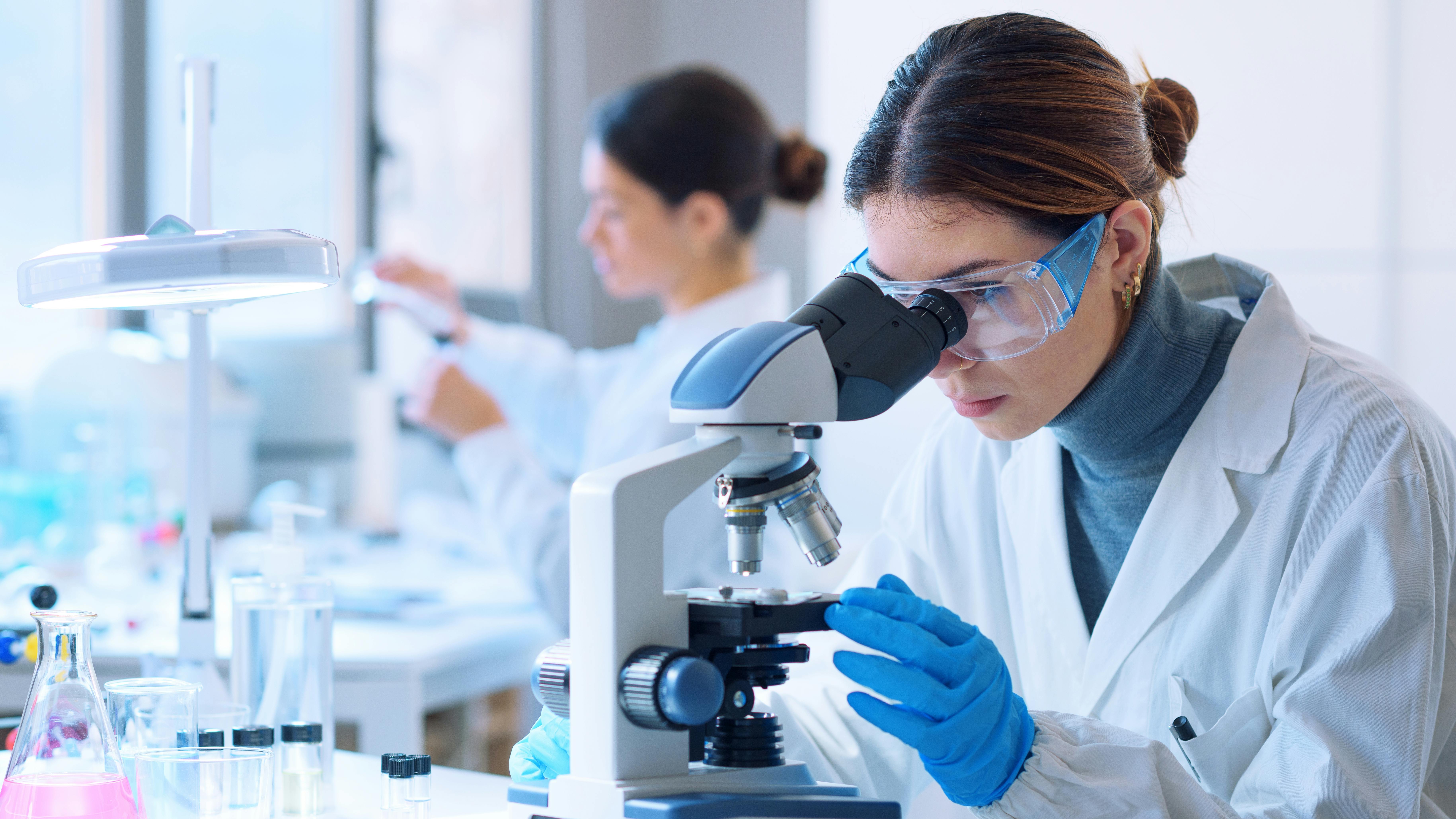 Young scientists conducting research investigations in a medical laboratory, a researcher in the foreground is using a microscope