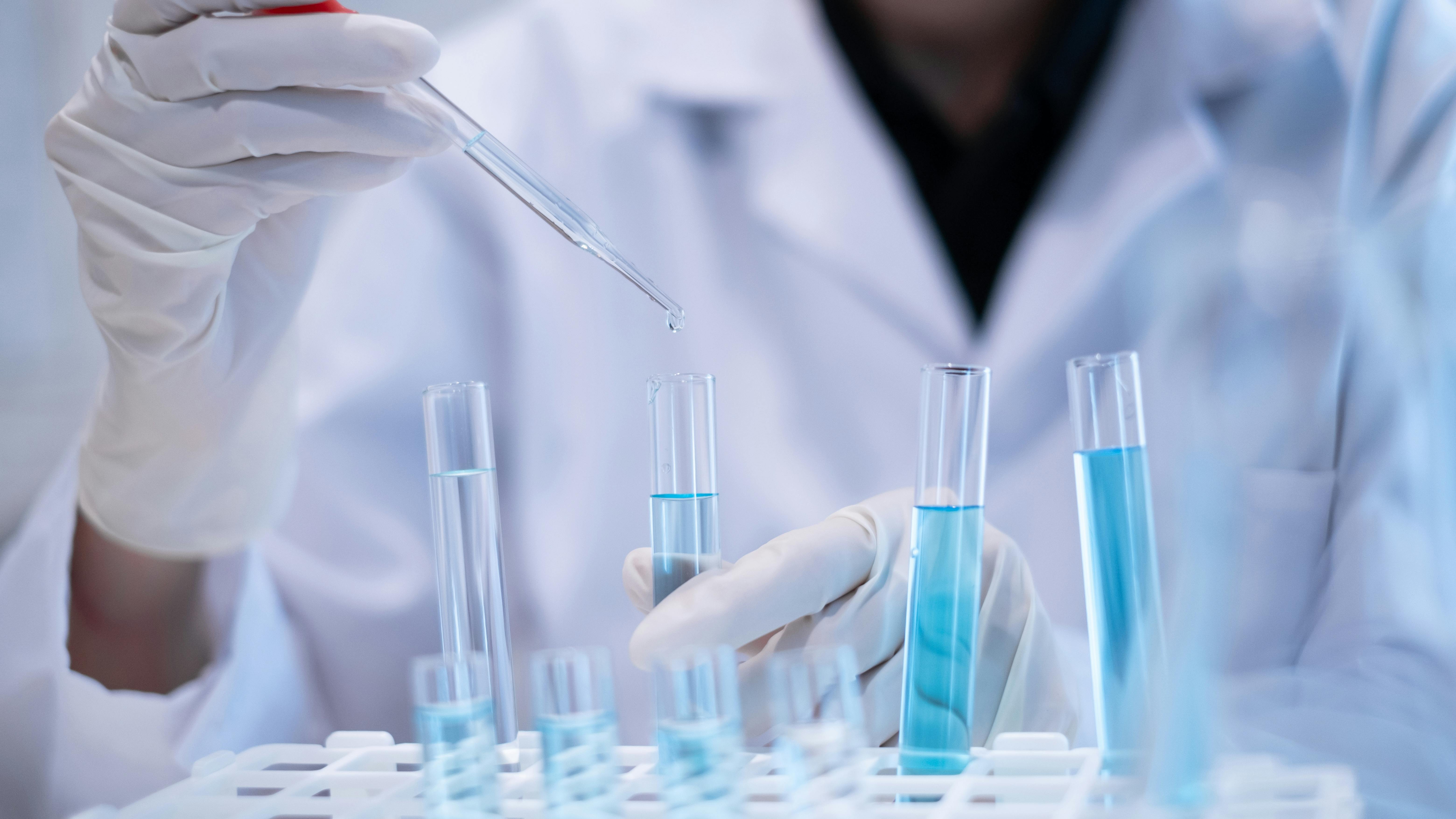 gloved hands hold test tube and dropper