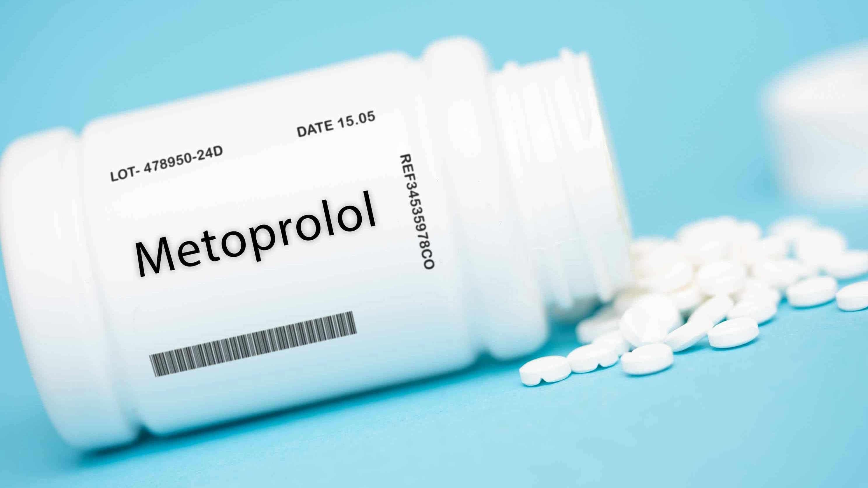 pill bottle labeled Metoprolol, on its side with pills around it, blue background