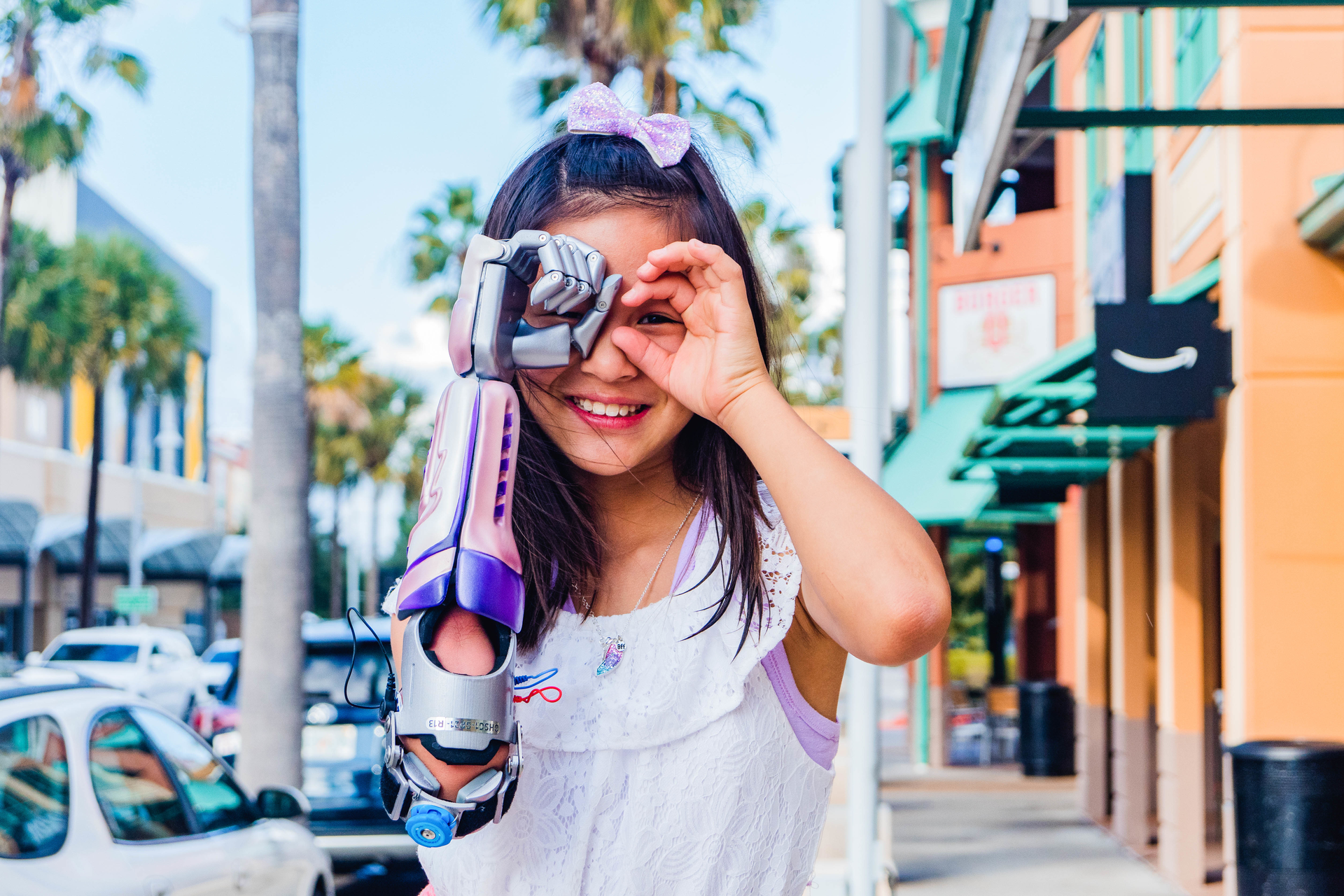 A young girl poses for a picture while using a bionic arm designed for her by Limbitless.