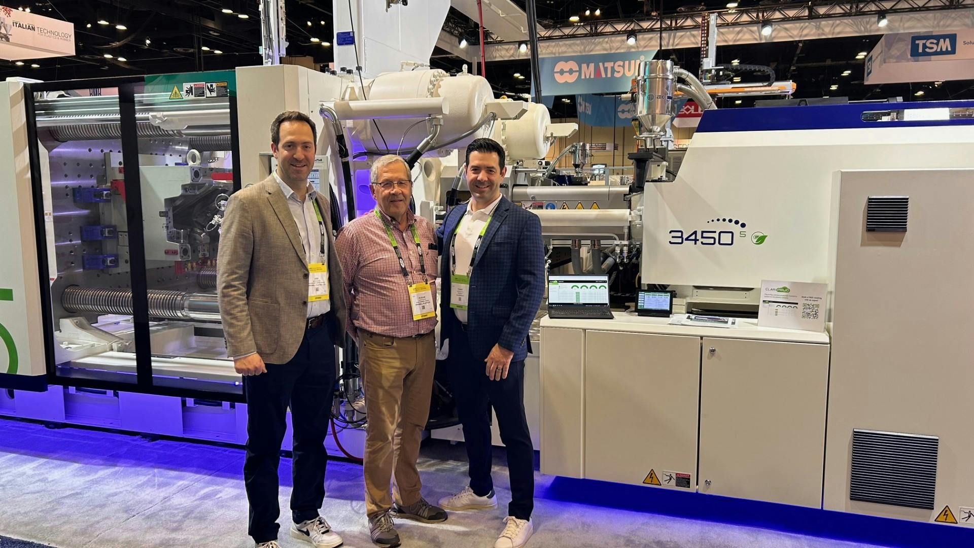 Erik Desrosiers, left, and Frank Desrosiers, right, flank their father, R&eacute;jean Desrosiers, in front of an injection molding machine at NPE. The three men co-founded ClariProd, a company now marketing a machine-monitoring system of the same name,