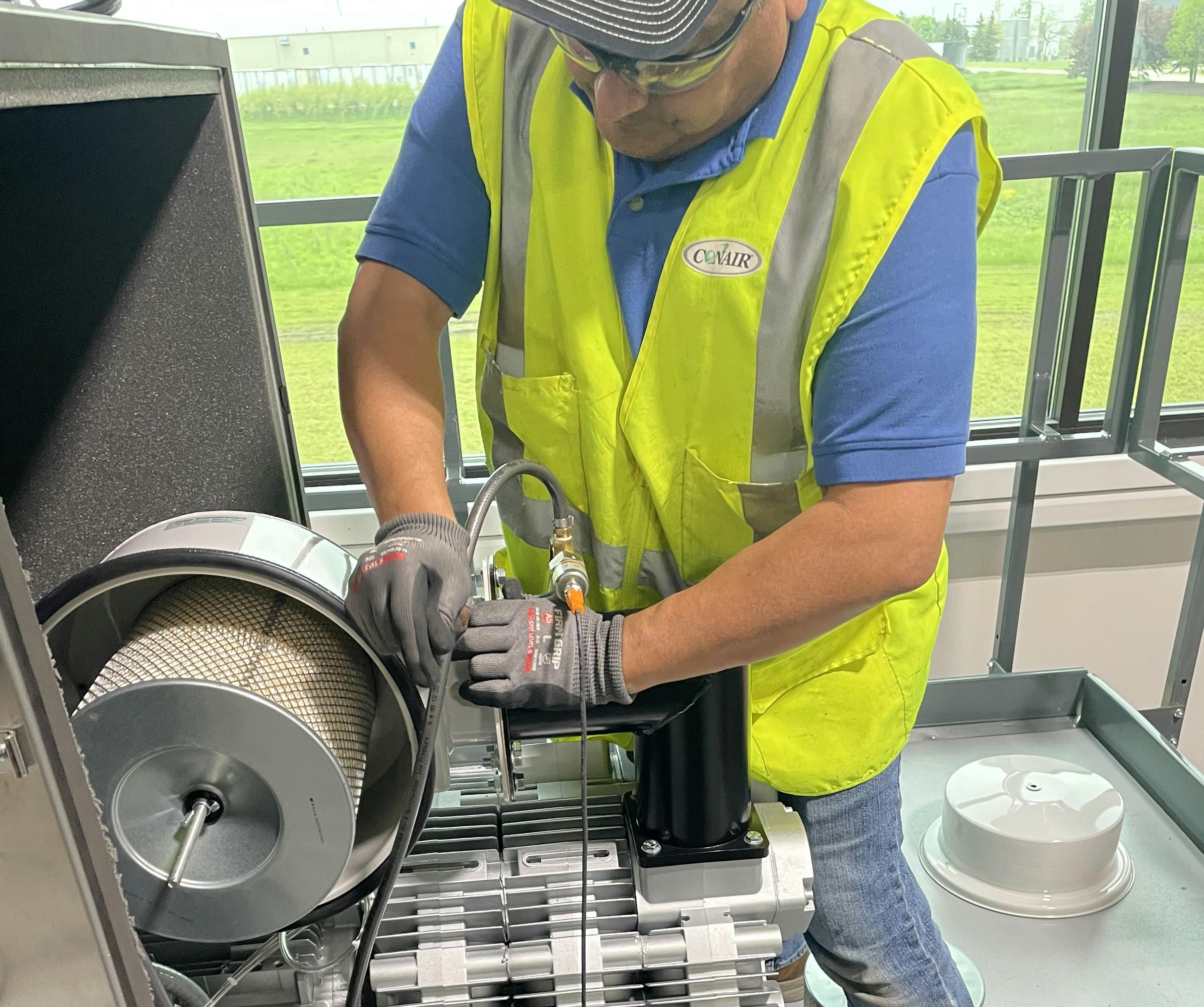 As part of a SureLaunch visit, a Conair technician inspects and validates the installation of a large central vacuum pump prior to successful commissioning and startup of a conveying system.