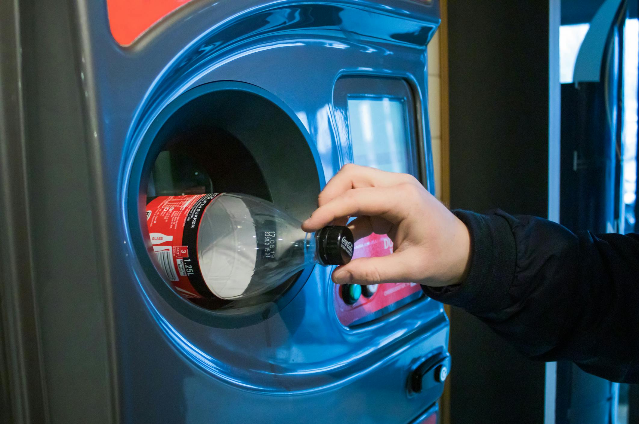 A person returns a plastic bottle to a recycling receptacle.