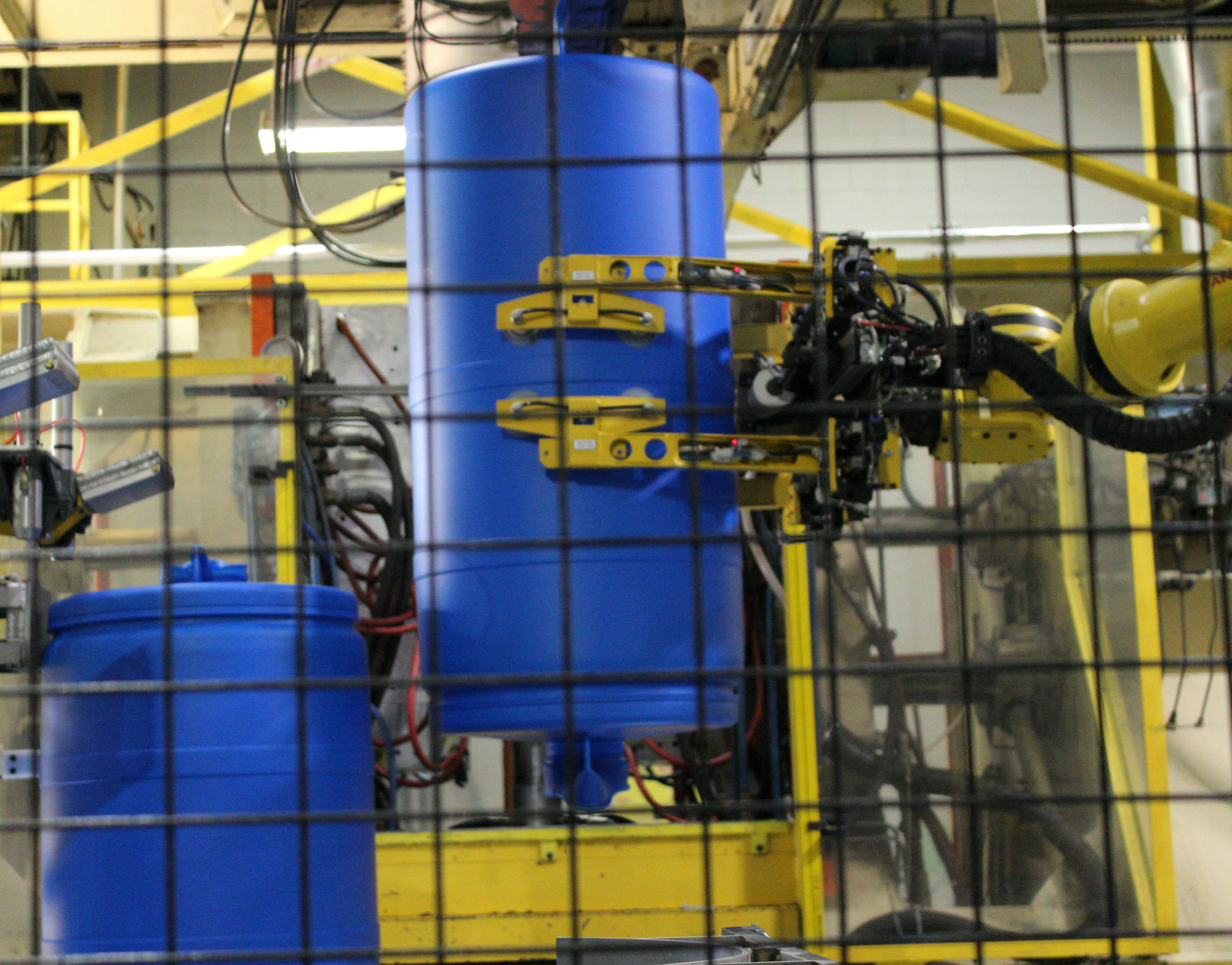 A robot provided by Minatech interfaces with a blow molding machine producing drums at Greif.